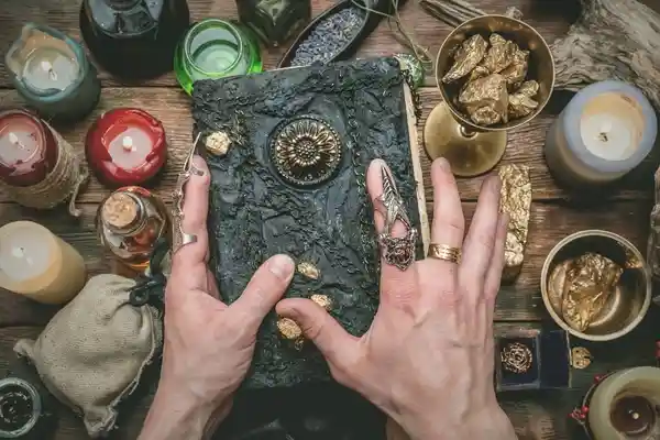 صورة تحتوي على يد تحمل كتاب و شموع و أحجار سحر الكراهية