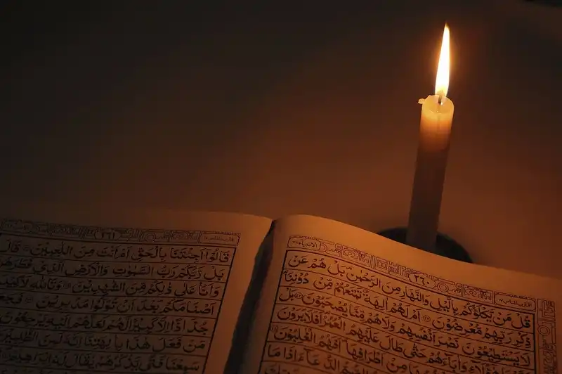 صورة تحتوي على كتاب وشمعة شيخ روحاني عماني
